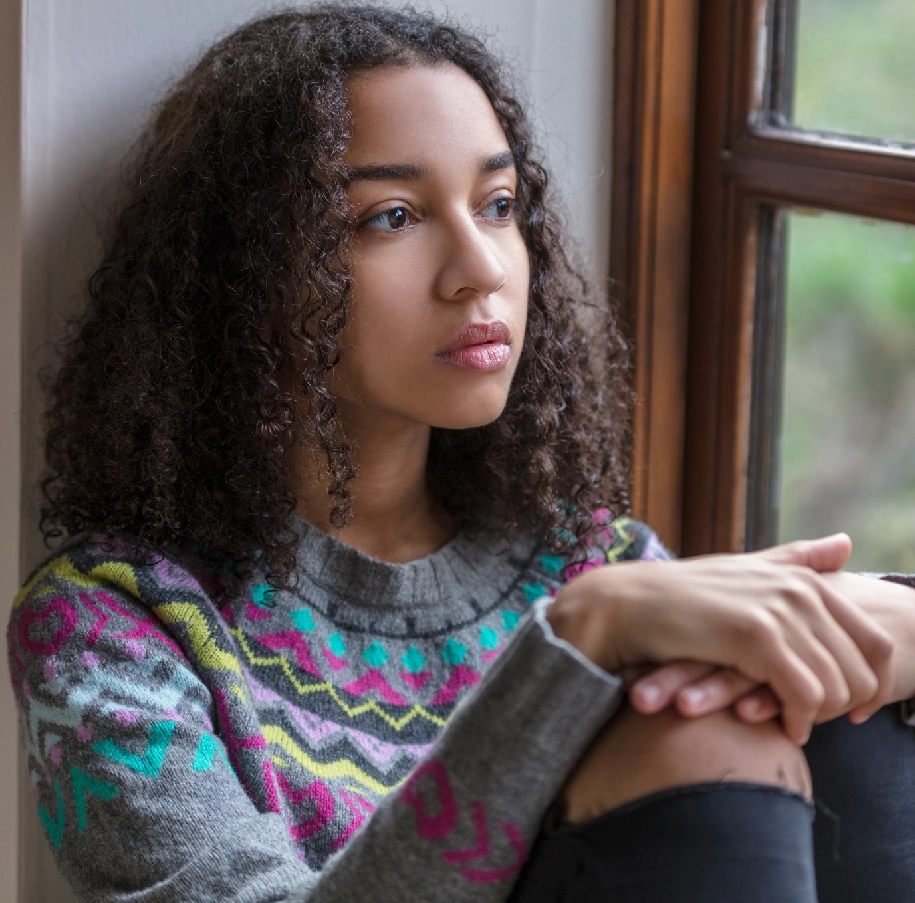 Young woman with curly hair looks out window.