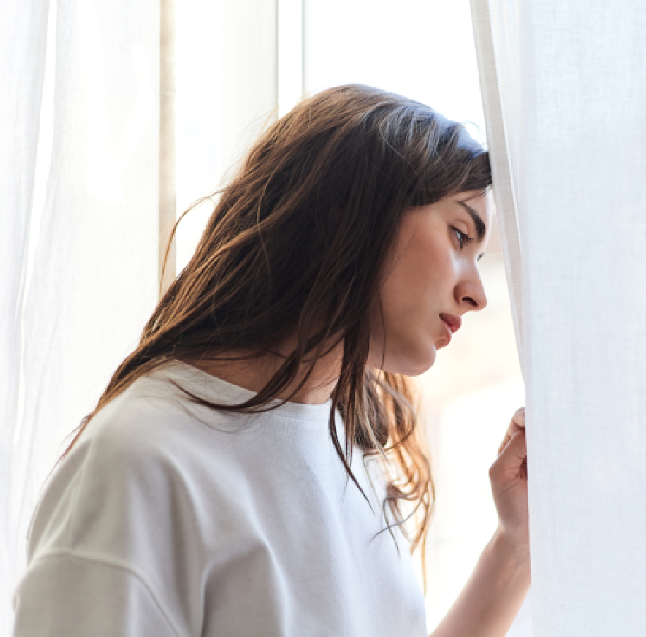 Woman looking out window with sad expression.